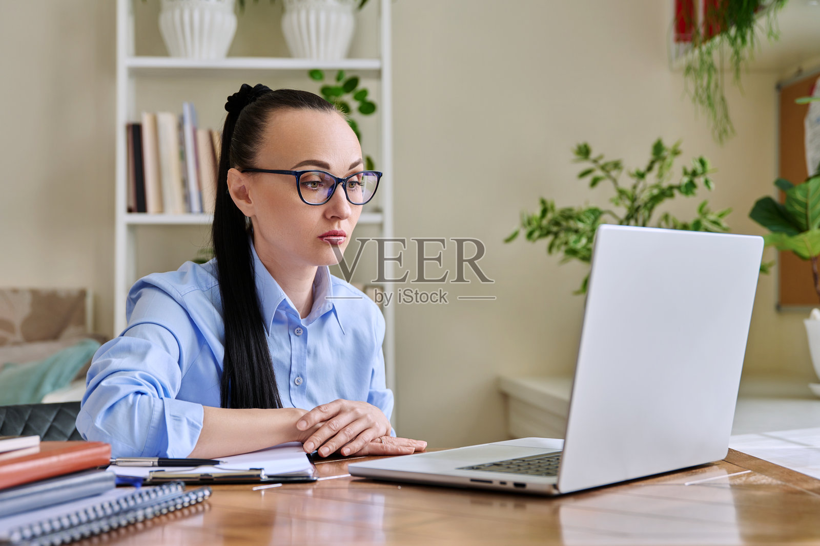 中年女性在家办公室使用电脑，面对摄像头交谈。照片摄影图片