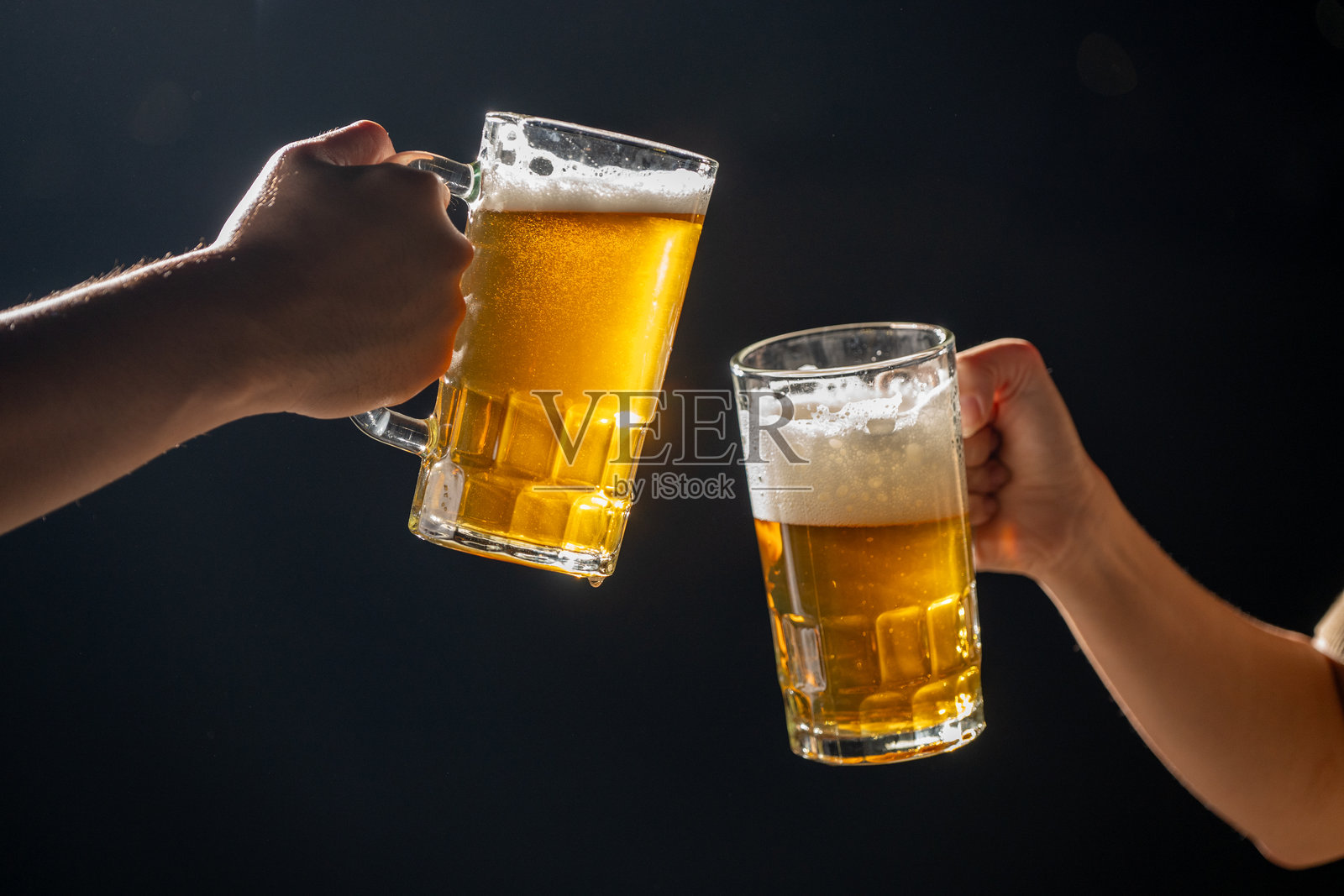 两只手举起泡沫溢出的啤酒杯，热烈地祝酒庆祝啤酒节。啤酒从杯中溢出，增添了这个经典德国节日的节日气氛。照片摄影图片