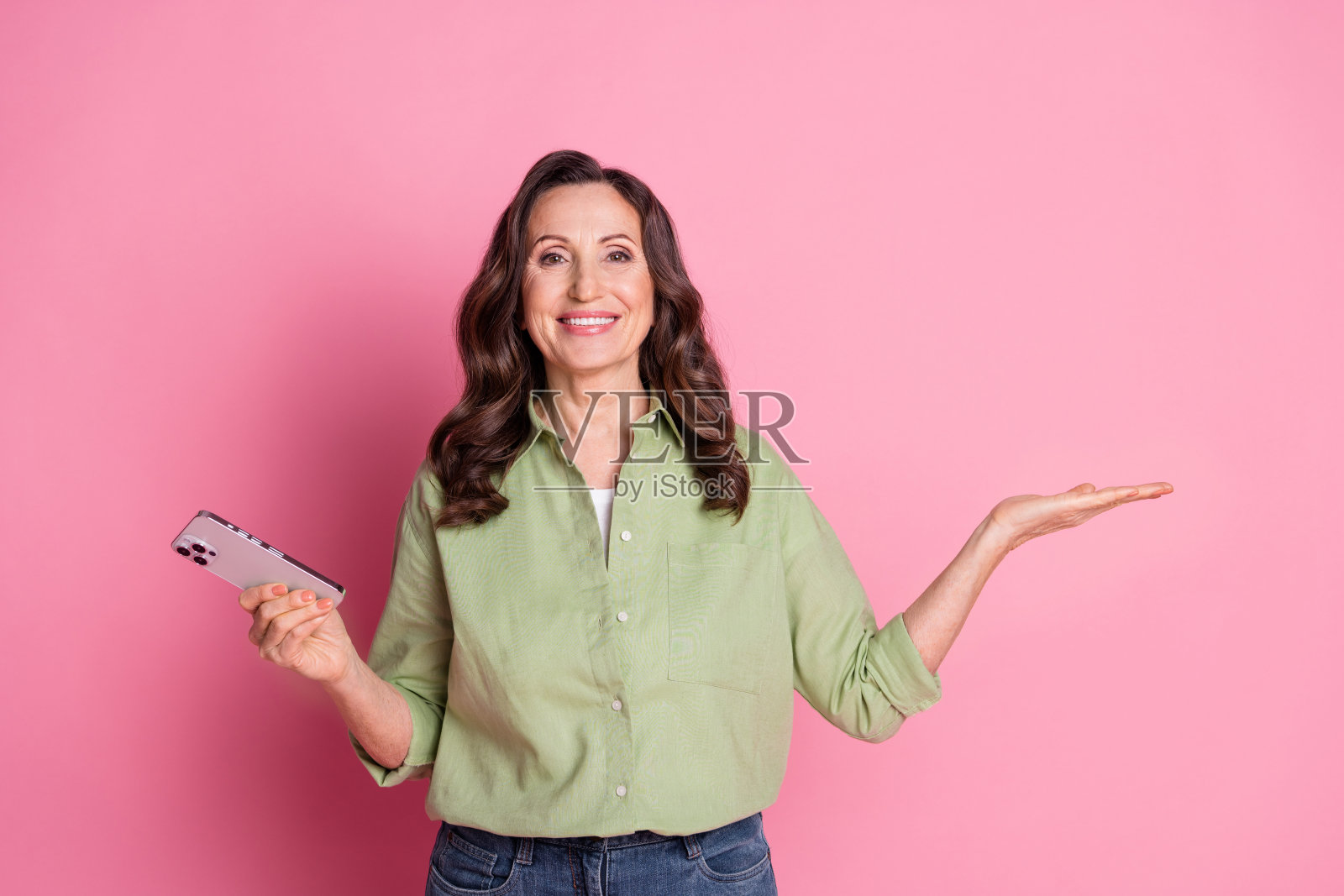 穿着衬衫的快乐美丽老年女销售员手持租房手机应用程序，背景为粉色。照片摄影图片