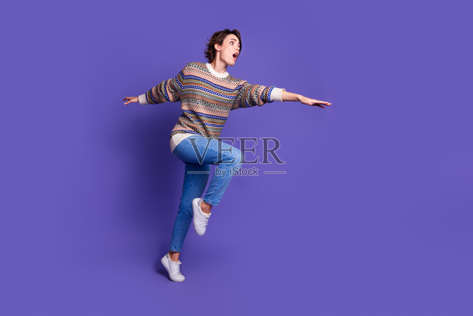 一位惊恐的漂亮女性穿着时尚服装，在紫色背景下空旷的空间中奔跑。照片摄影图片