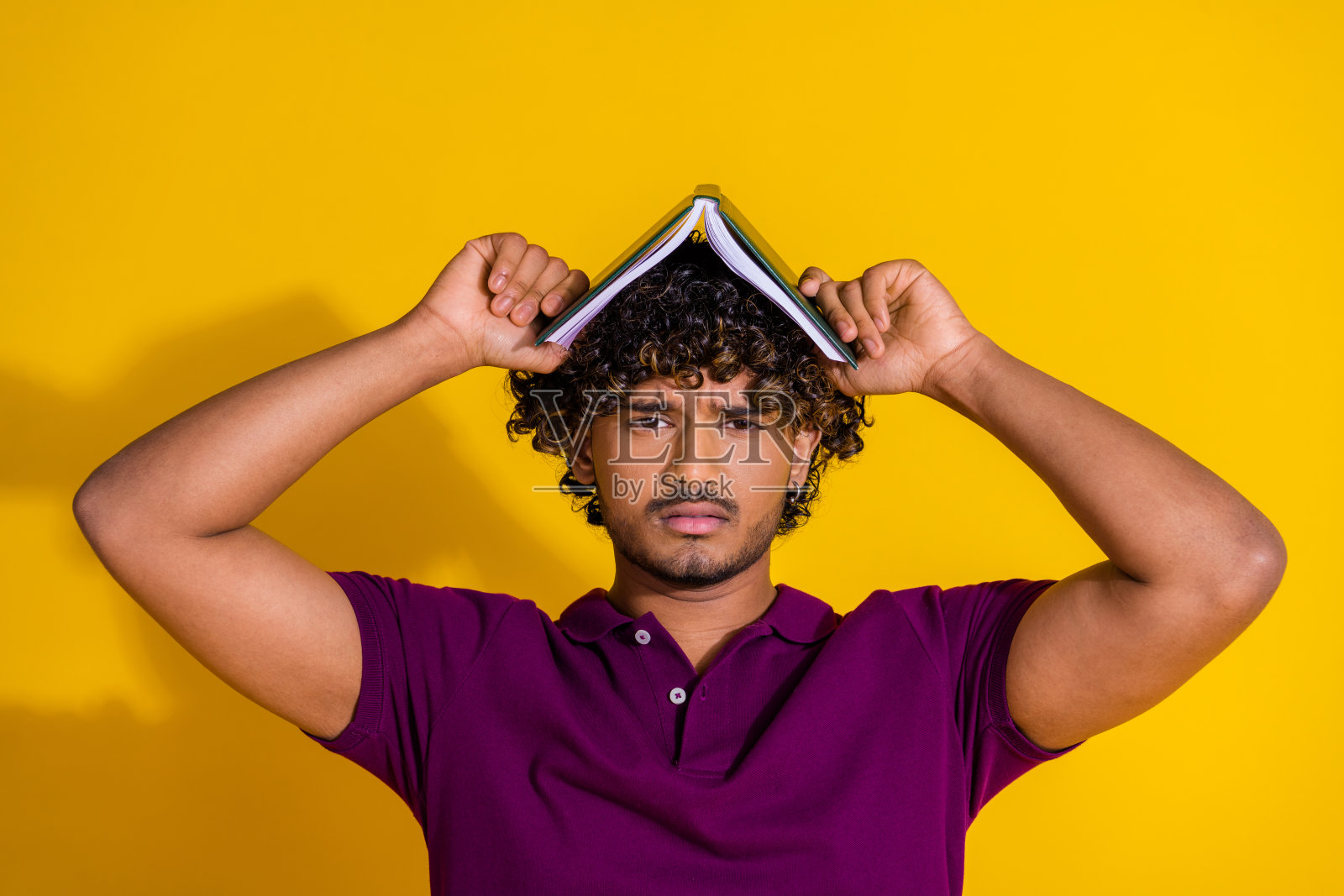 年轻男子的照片肖像，情绪低落，穿着时尚的紫色服装，站在屋顶上，背景为黄色。照片摄影图片