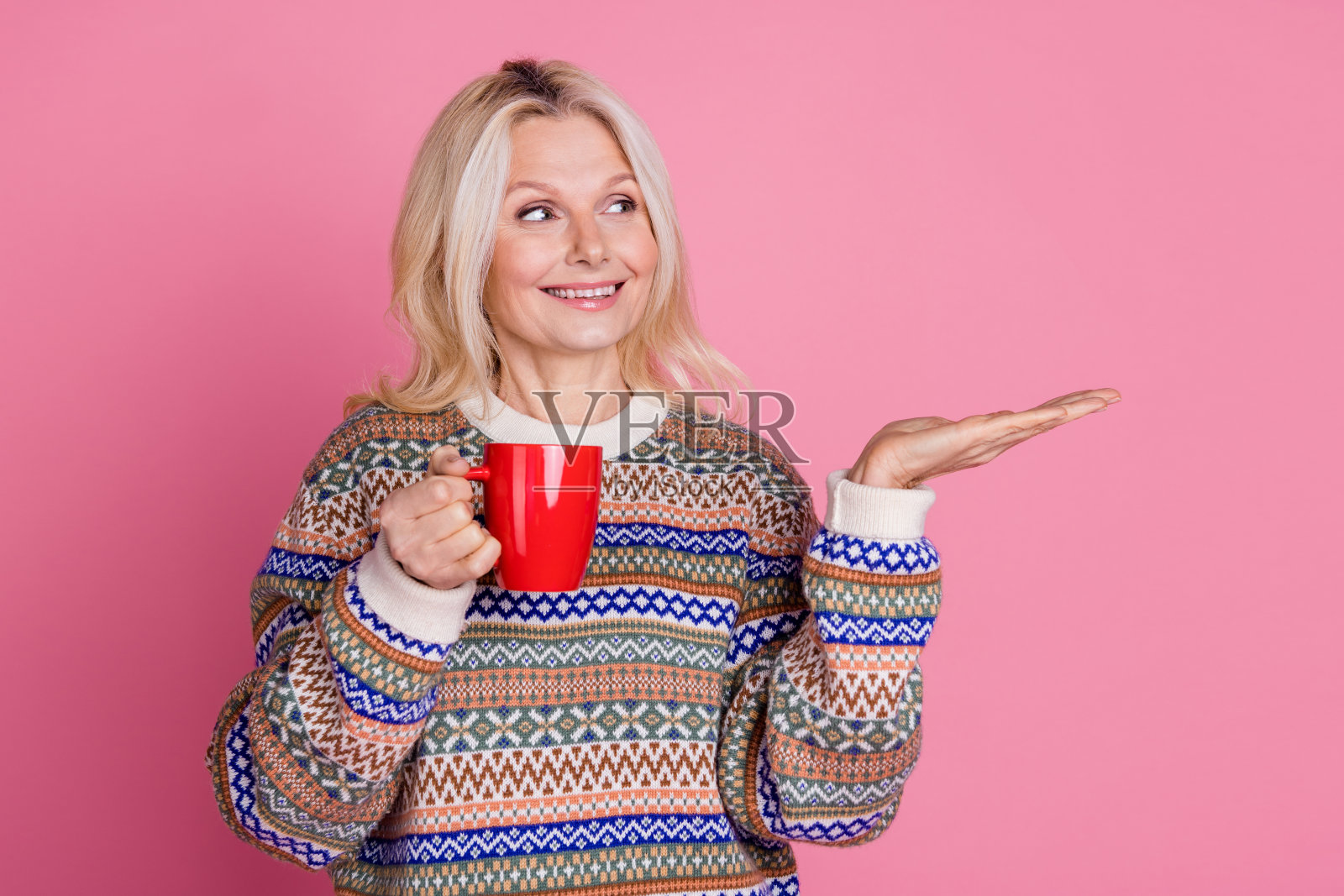 漂亮的老年女士手持杯子，穿着毛衣，背景为粉色，空白空间。照片摄影图片