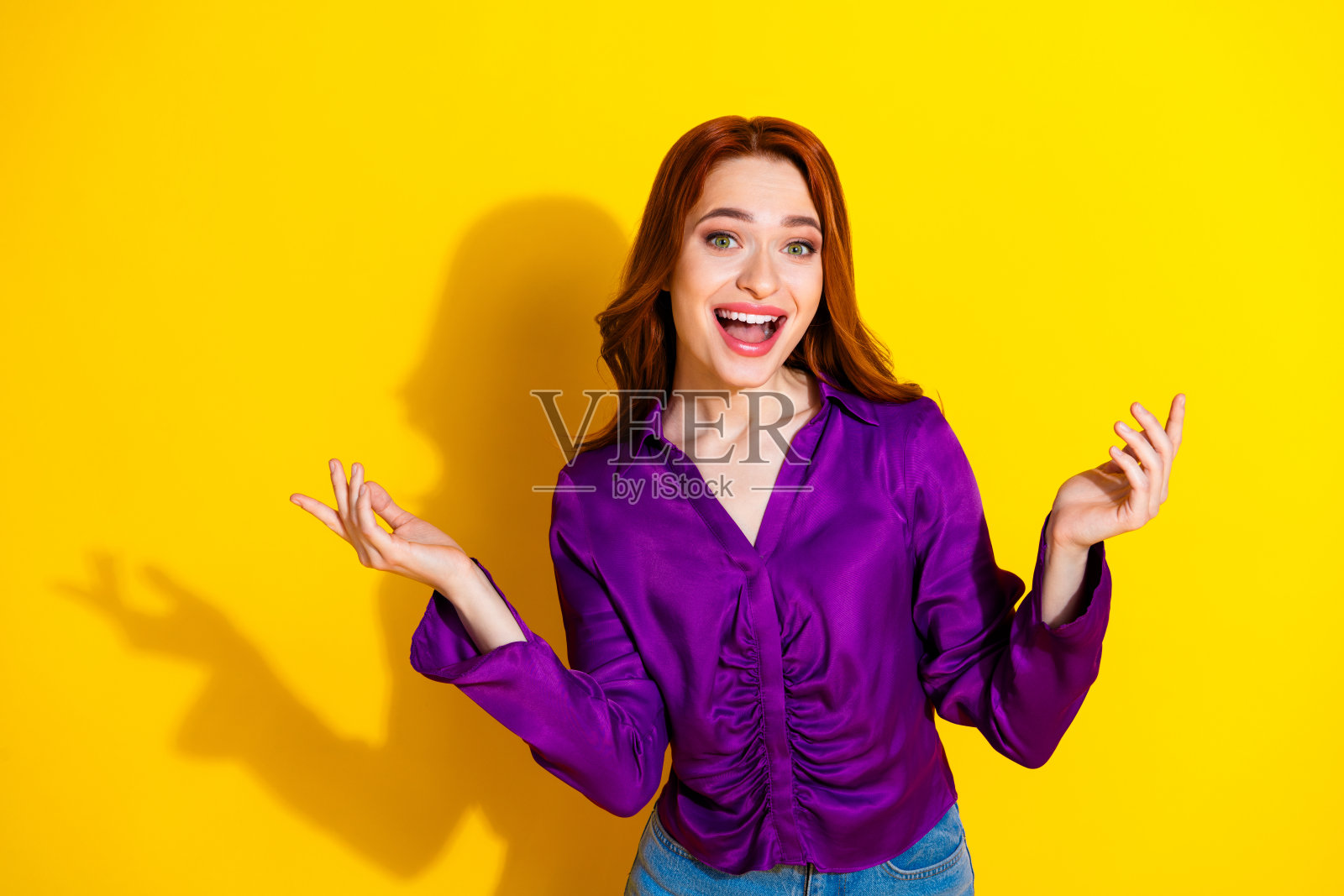 穿着时尚紫色服装的漂亮年轻女孩兴奋地举起双手，背景为黄色。照片摄影图片
