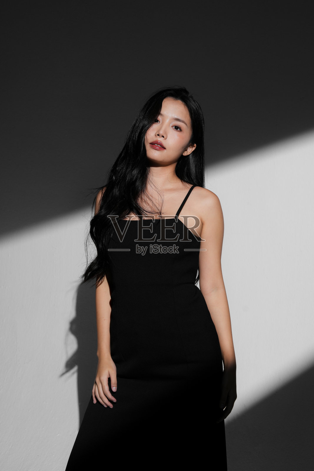 年轻女性身穿黑色连衣裙的时尚肖像，背景为光影交错。照片摄影图片