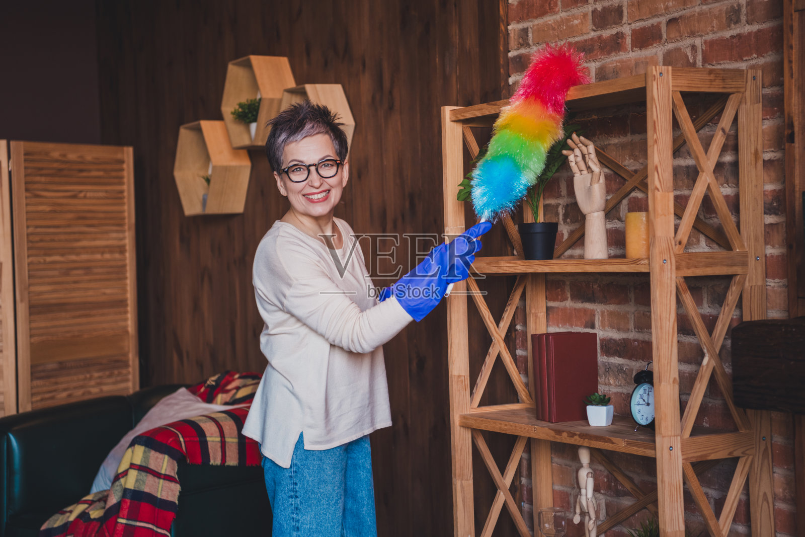 迷人的老年女性，短灰发，穿着休闲毛衣，在家中清理书架。照片摄影图片