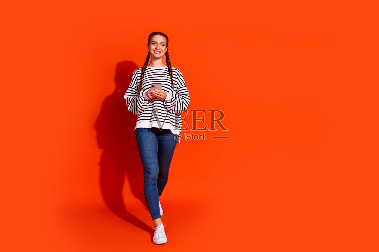 年轻女性穿着休闲时尚的条纹服装，背景为鲜艳的橙色，展现出风格与自信。照片摄影图片