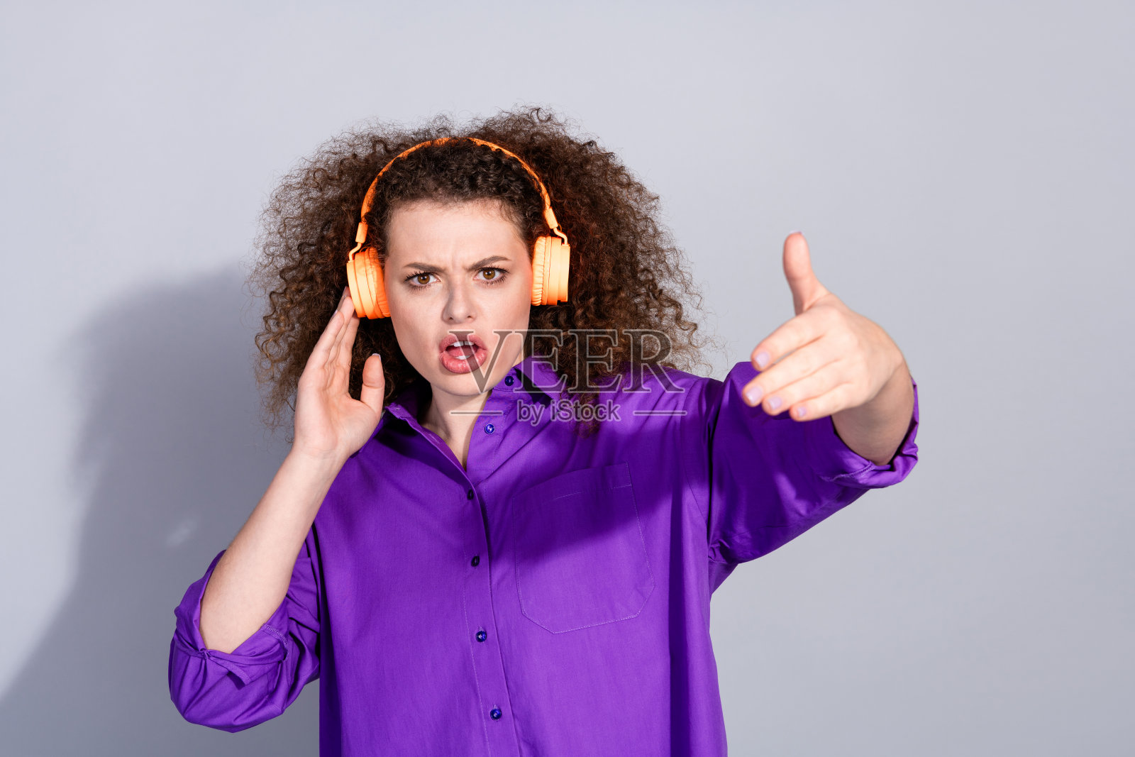 年轻女性穿着紫色衬衫，戴着耳机跳舞，背景为灰色。照片摄影图片