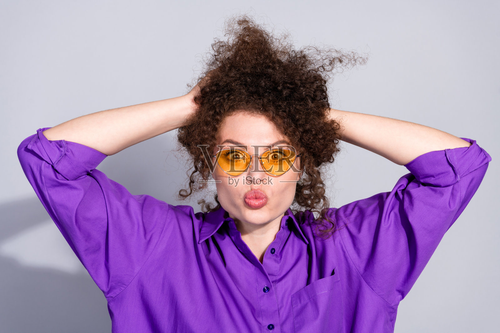 年轻漂亮的女性穿着紫色衬衫，手握头发，亲吻嘴唇，背景为灰色。照片摄影图片