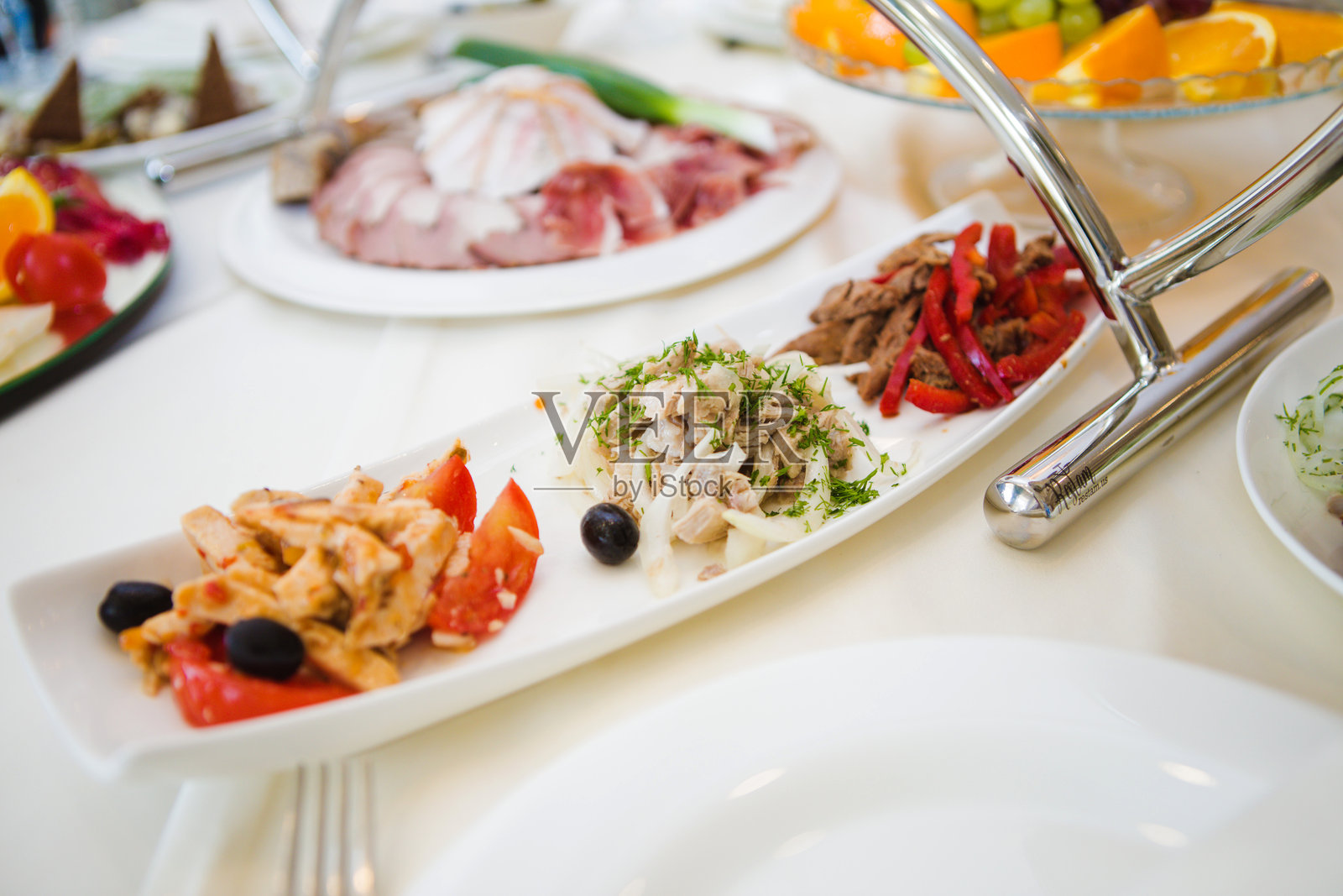 一个白色盘子上摆放着各种食物，包括肉类、蔬菜和橄榄。盘子放在桌子上，旁边还有其他盘子和餐具。照片摄影图片