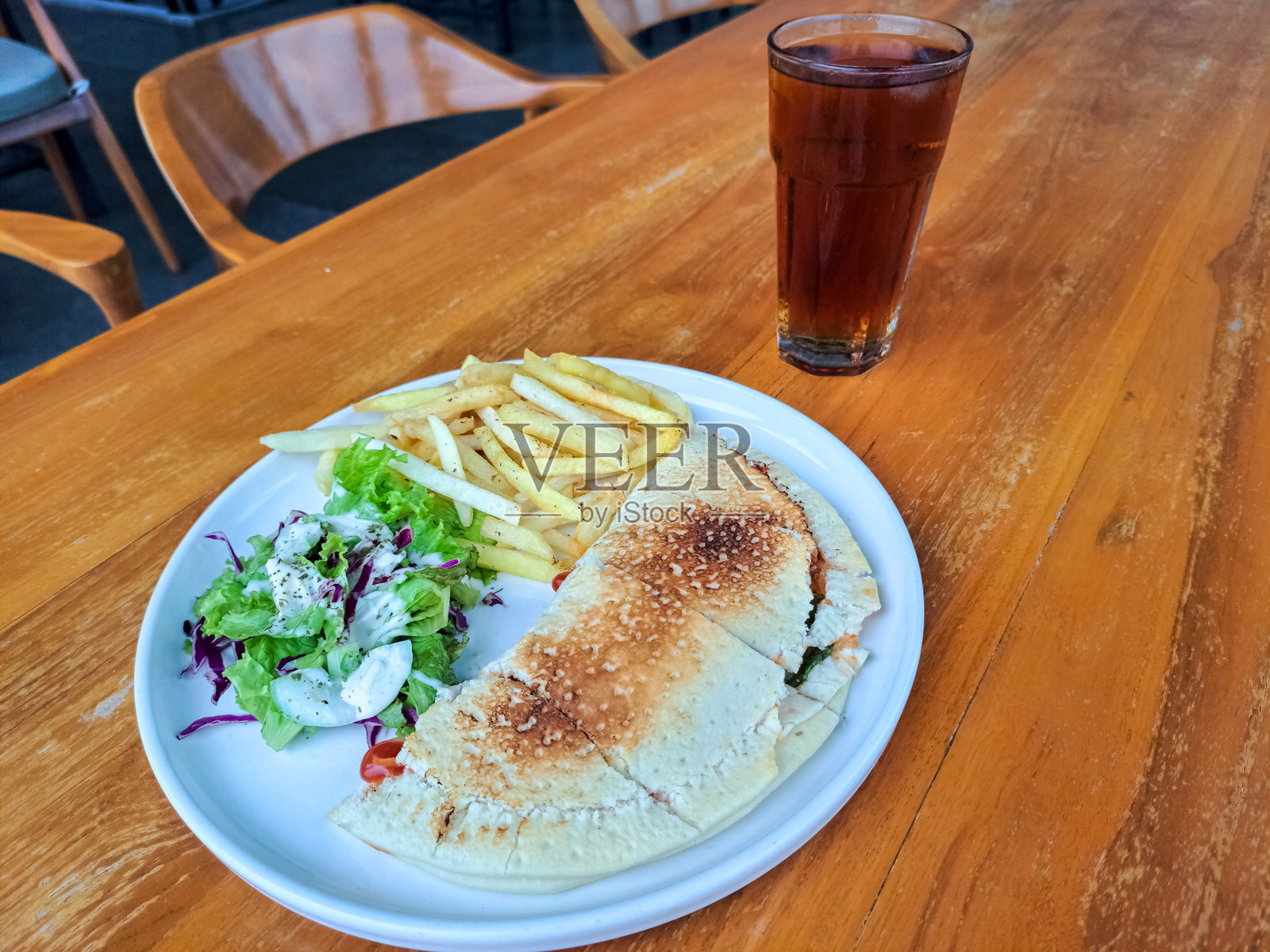 美味的意大利肉馅饼，配有普朗托、培根和马苏里拉奶酪，外裹比萨饼面团，旁边有沙拉和薯条。新鲜的冰茶装在玻璃杯中。食品和饮料菜单。照片摄影图片