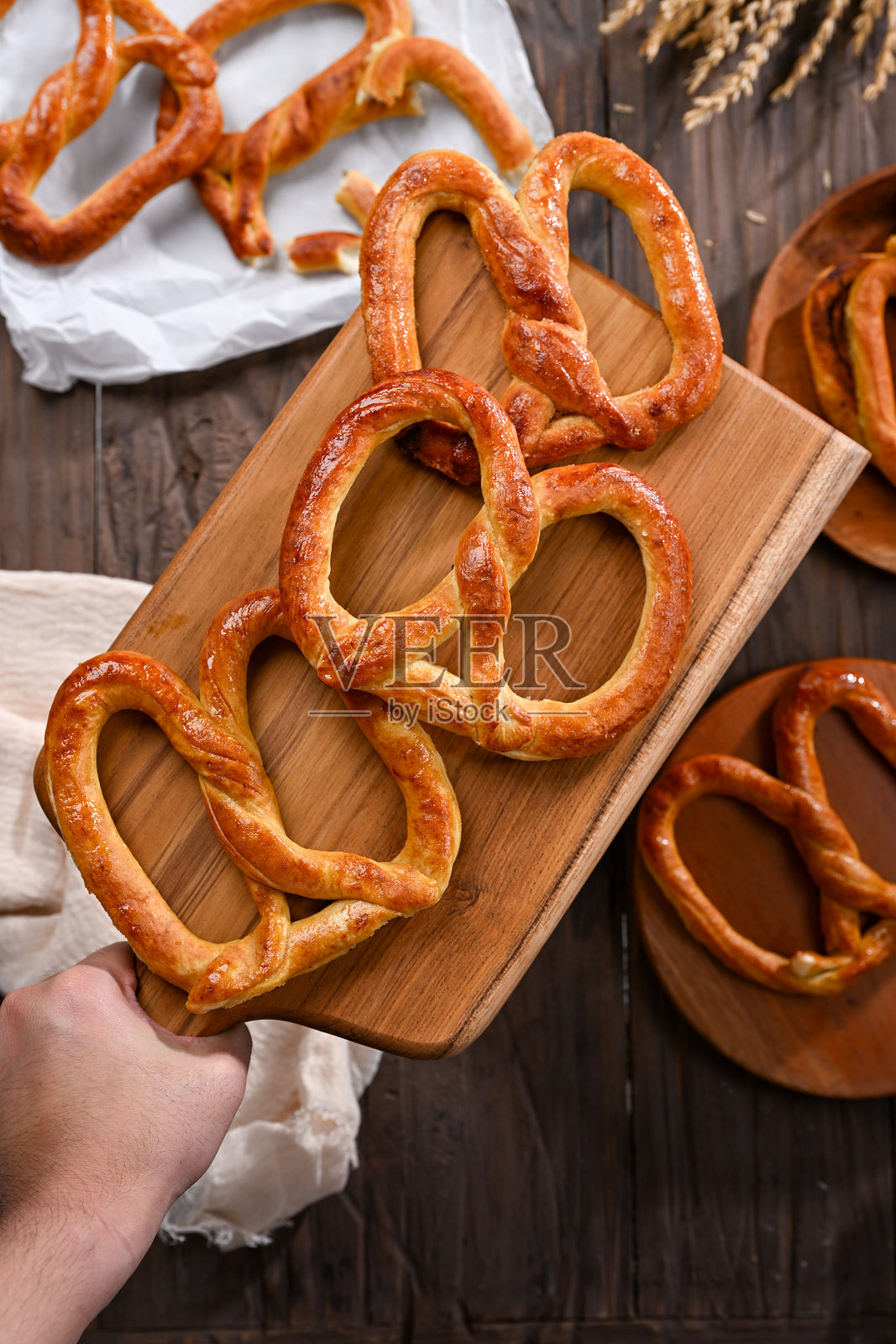 一批新鲜的金棕色椒盐卷饼静静地放在木砧板上，随时可以上桌。温暖酥脆的口感和简单的摆盘使其成为完美的小吃，适合分享。照片摄影图片