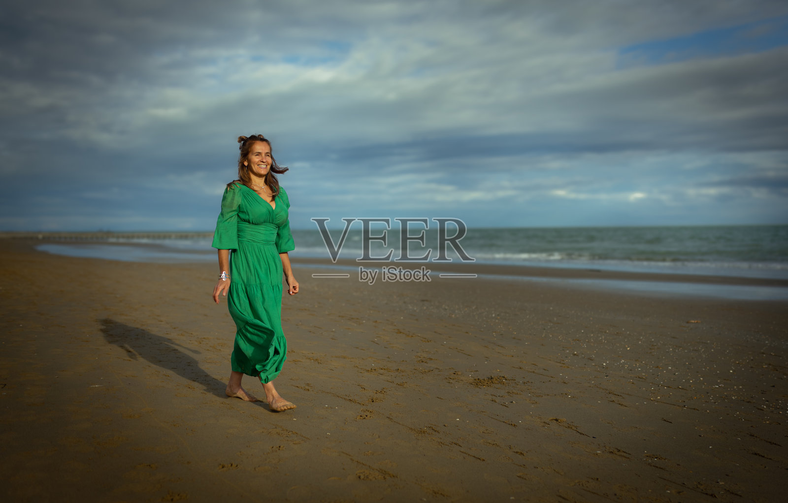穿着绿色裙子的女人在沙滩上漫步，享受夏日时光照片摄影图片