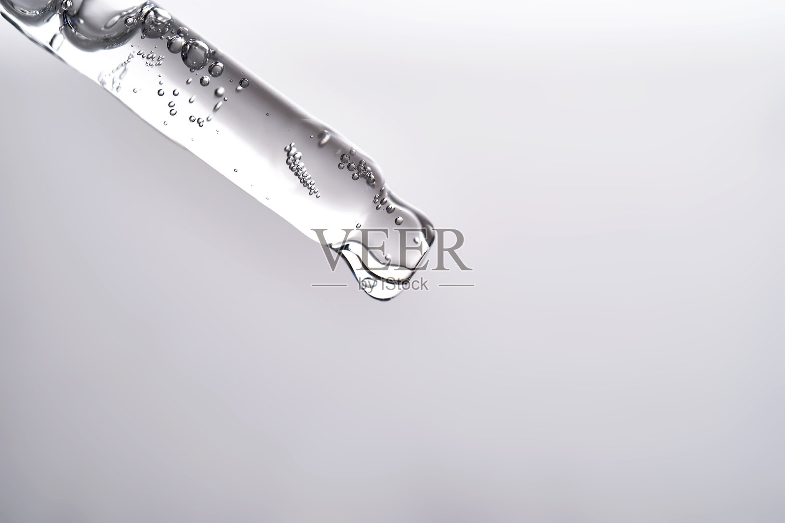 灰色背景上滴管正滴出面部精华液。照片摄影图片