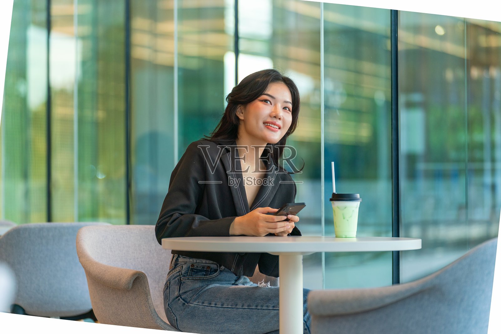 年轻的亚洲华裔女商人在现代咖啡馆里坐着，使用智能手机并微笑。照片摄影图片
