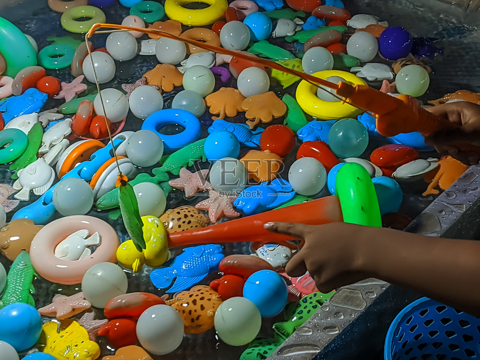 一个孩子的手灵巧地操控着玩具钓鱼竿，在五颜六色的塑料玩具池中游玩照片摄影图片