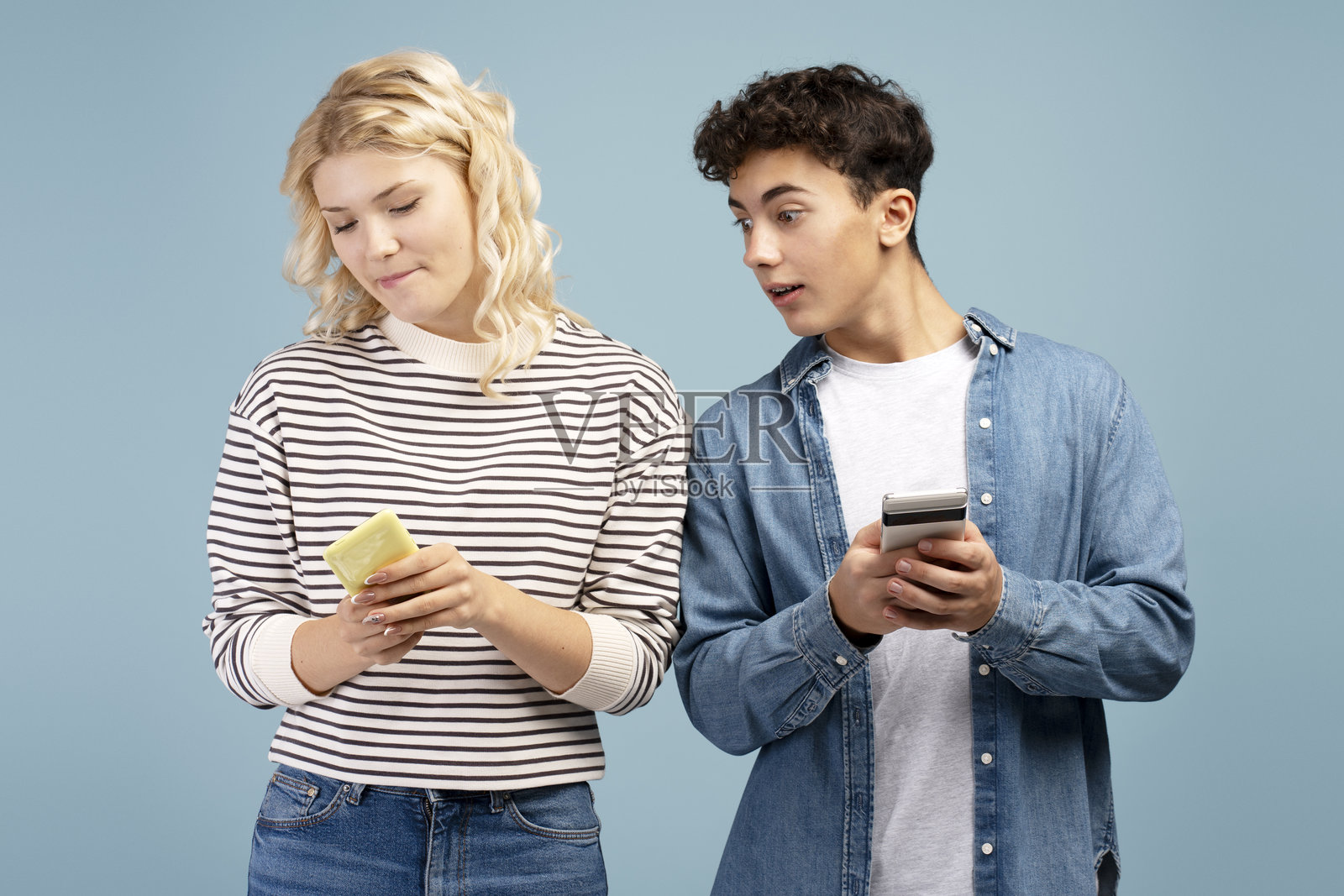 年轻情侣的肖像，女友和男友手持手机，少年男孩在偷偷观察女孩。照片摄影图片