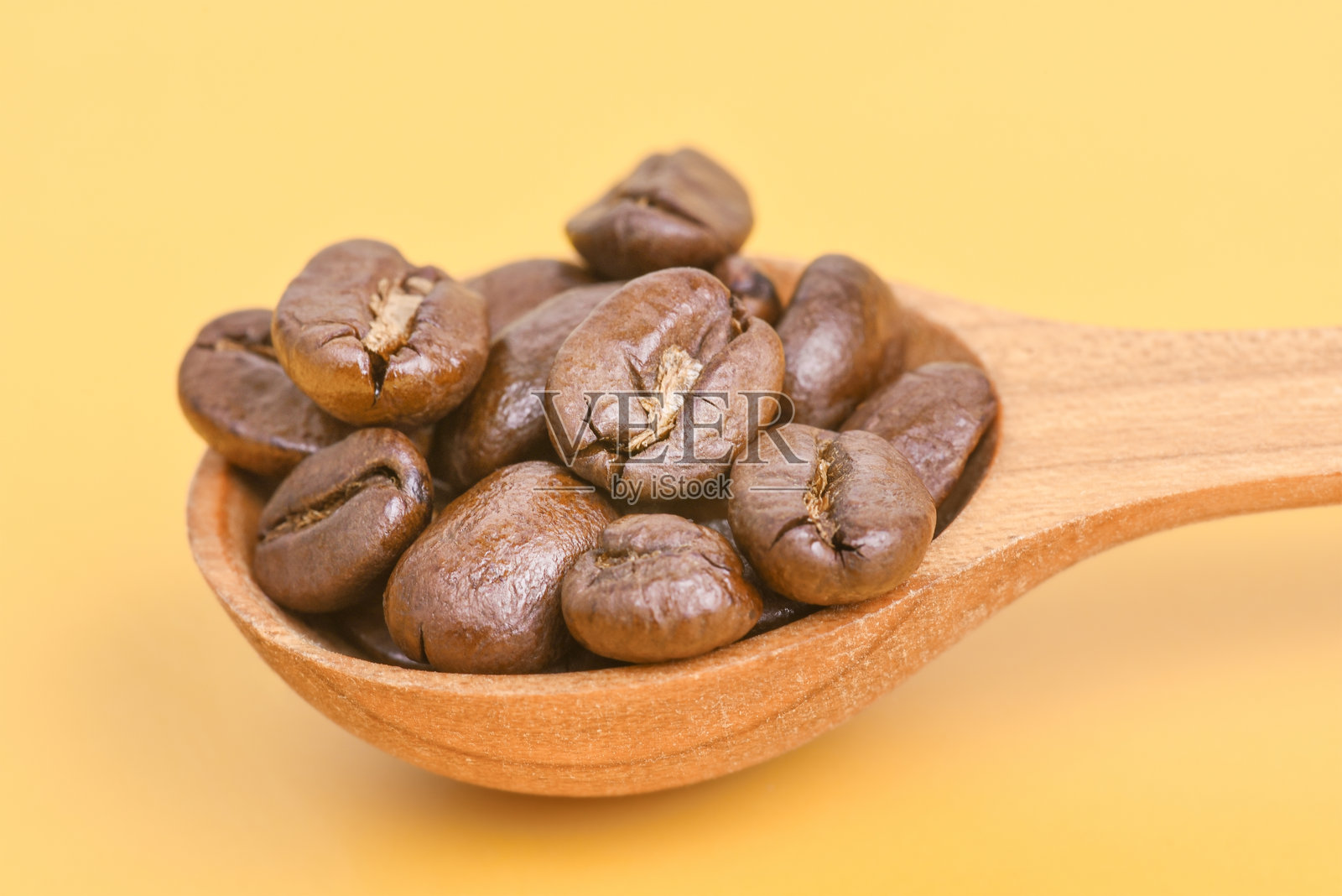 木勺与香气四溢的烘焙咖啡豆置于黄色背景上。照片摄影图片