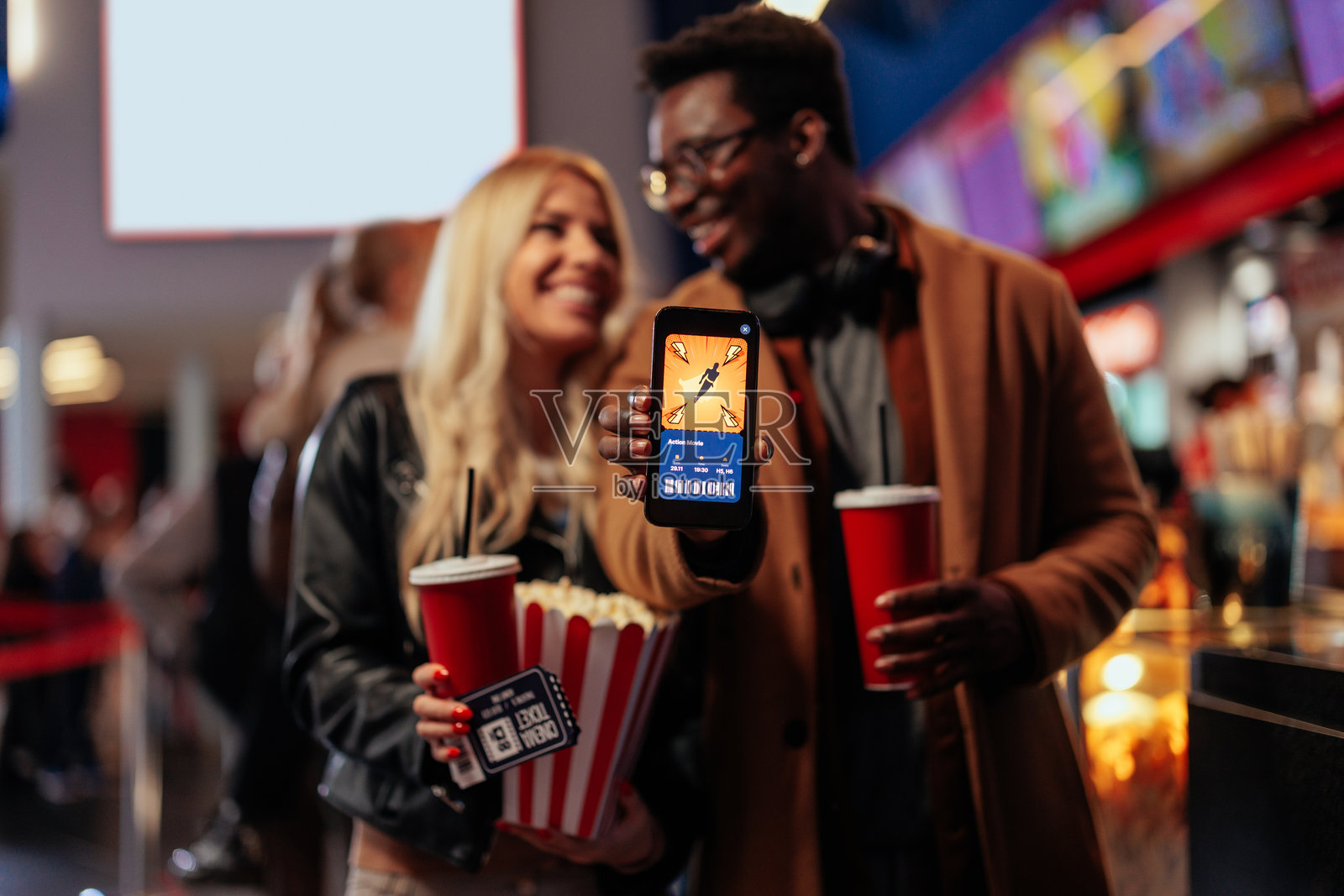 在电影院里使用手机应用的快乐情侣。照片摄影图片