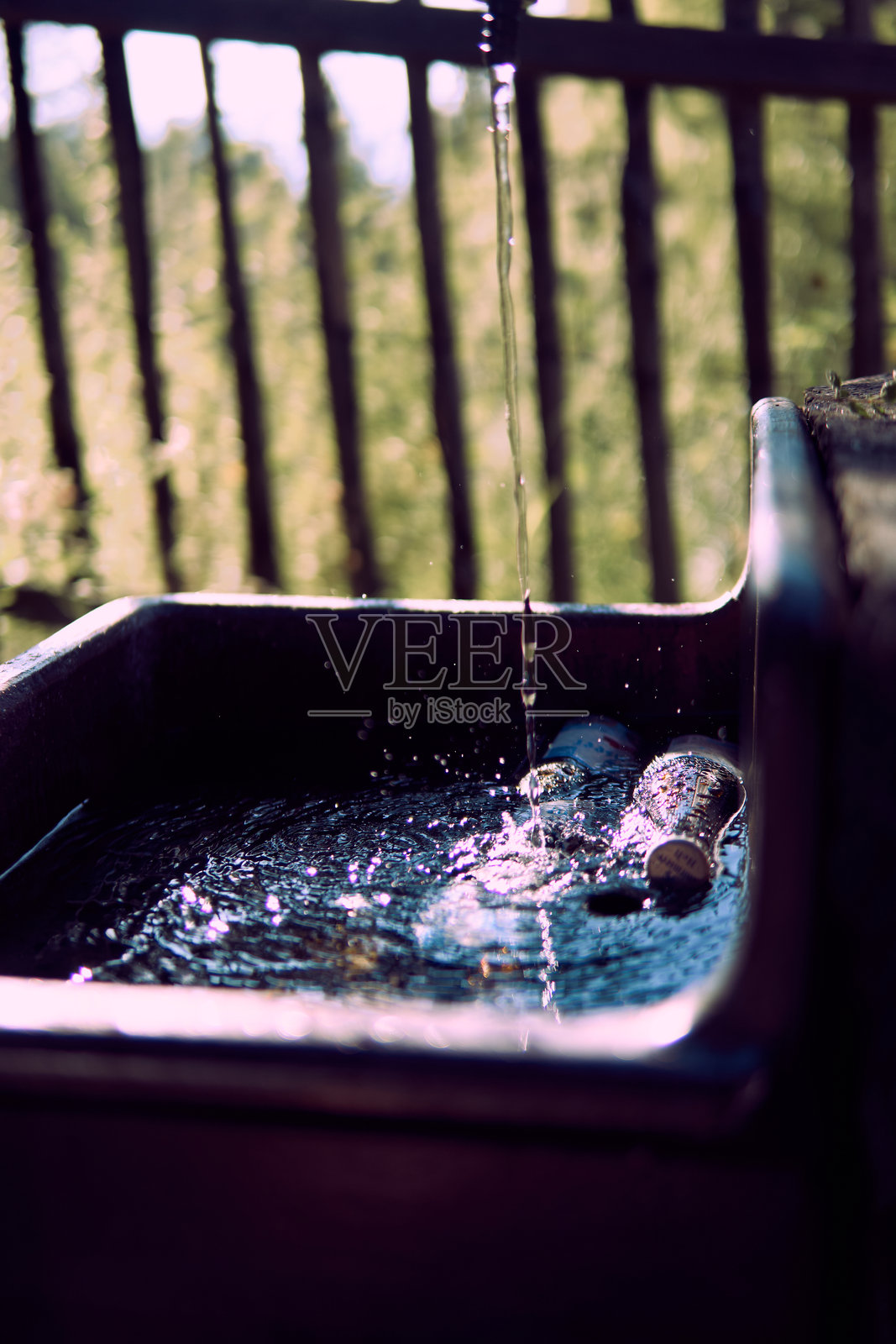 水从喷口涓涓流入一个黑暗的水池，四周被自然环绕，营造出宁静的户外环境。照片摄影图片