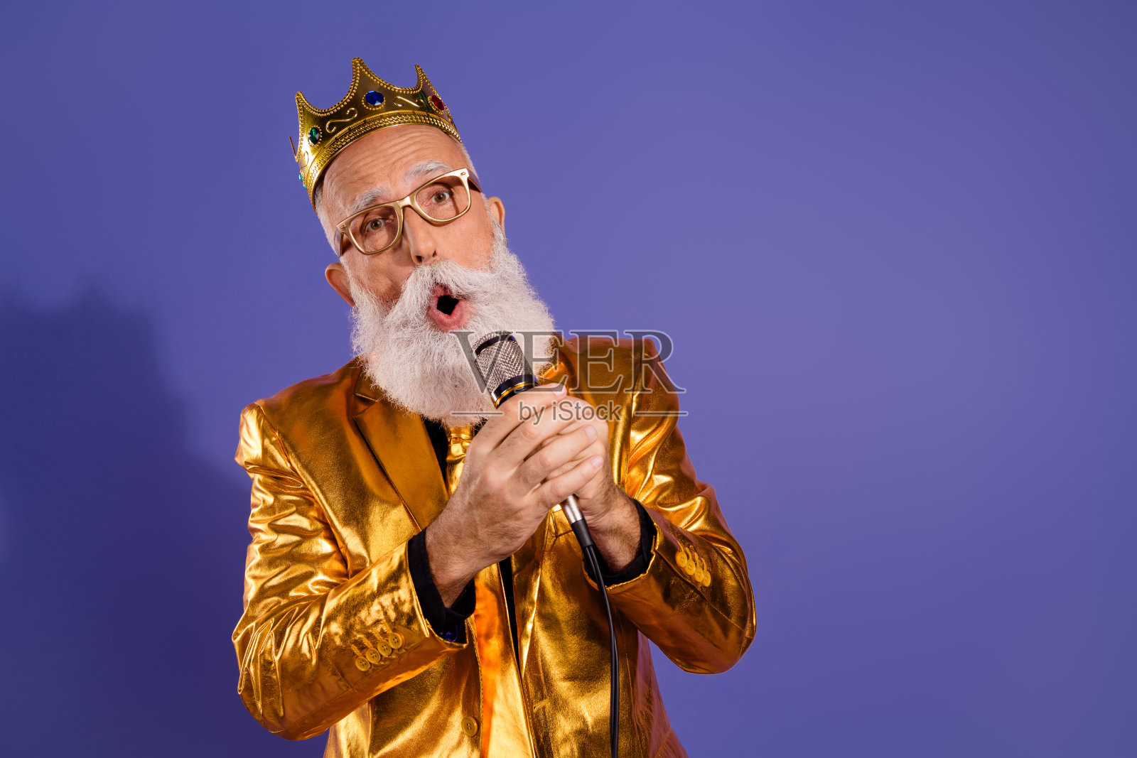 穿着华丽金色服装的老派男子在紫色背景下独自唱卡拉OK的照片肖像照片摄影图片