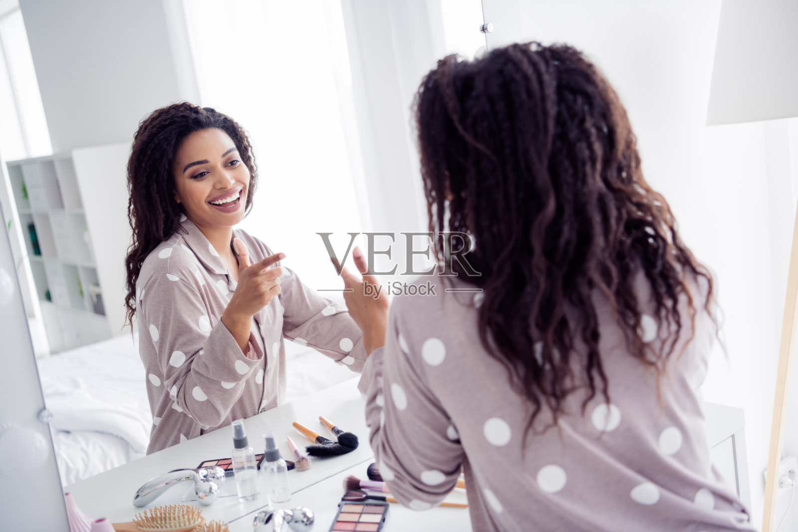 美丽的年轻女性穿着睡衣，在温馨的卧室镜子前享受晨间例行活动，沐浴在自然光中。照片摄影图片