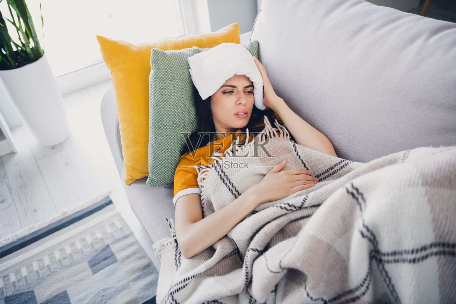 年轻女性在温馨的客厅里，裹着温暖的毯子，感到不适地休息在舒适的沙发上照片摄影图片