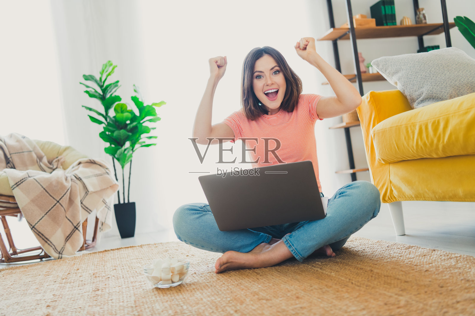 兴奋的年轻女性坐在家中，盘腿而坐，手里拿着笔记本电脑庆祝成功，短发造型。照片摄影图片
