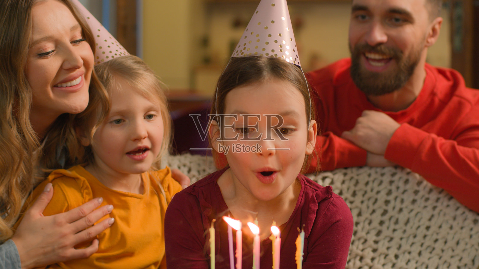 快乐的白人家庭为小女孩庆祝生日，孩子们在家里派对上吹灭蛋糕上的蜡烛，父母戴着节日帽子，惊喜地祝贺，充满欢乐。照片摄影图片