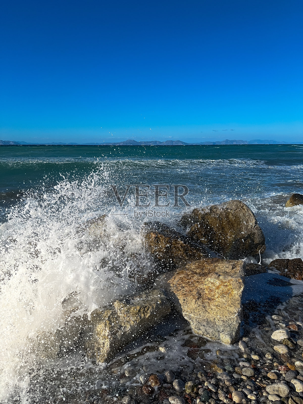 在明亮的白天，波浪拍打着岩石海岸，天空湛蓝。照片摄影图片