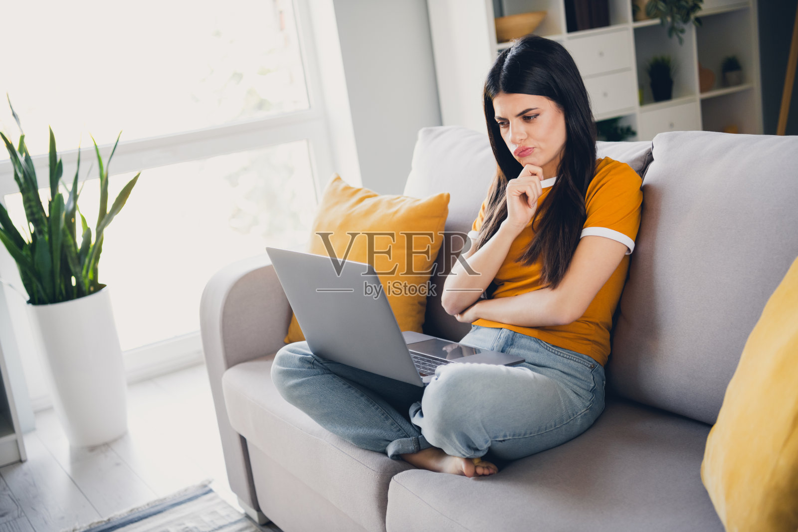 年轻的棕发女性坐在沙发上，悠闲地在家中思考屏幕。照片摄影图片