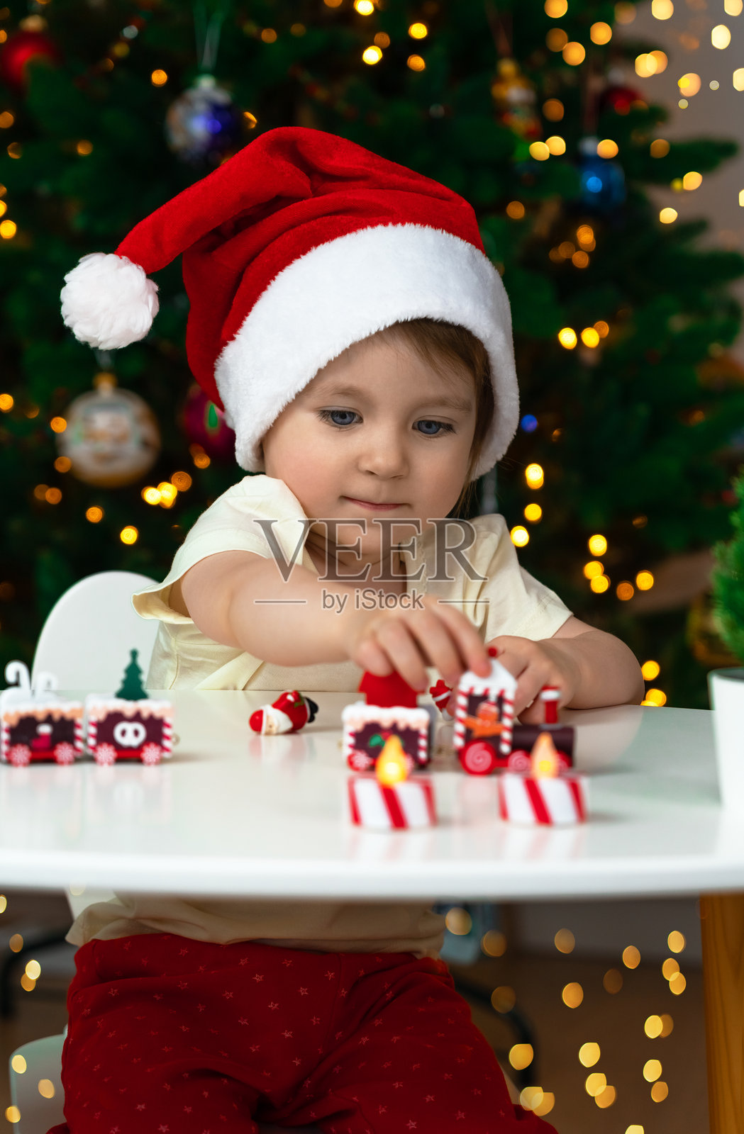 小女孩在圣诞树背景下玩玩具火车。新年礼物照片摄影图片