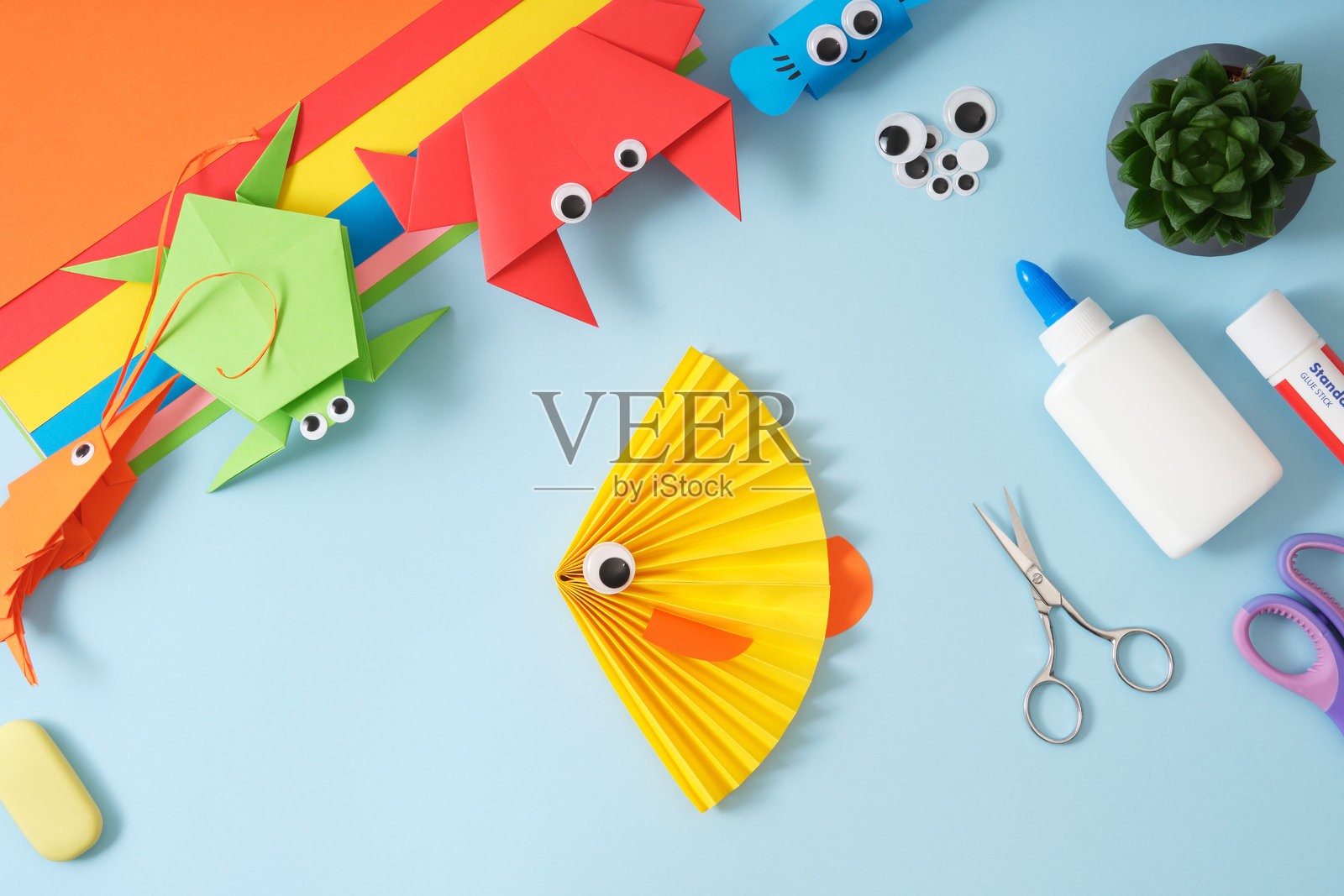 多彩的折纸工艺品：鱼、虾、蟹、乌龟。纸艺用品包括彩色纸张、胶水、剪刀，背景为蓝色。照片摄影图片