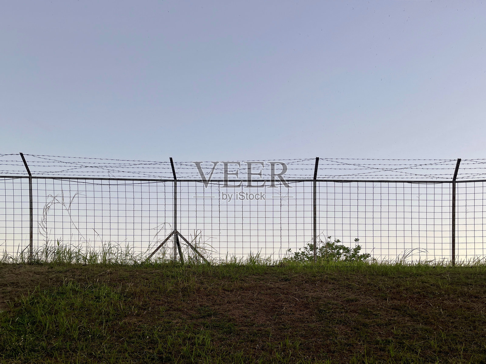 带刺铁丝网的围栏，草地和晴朗的蓝天照片摄影图片