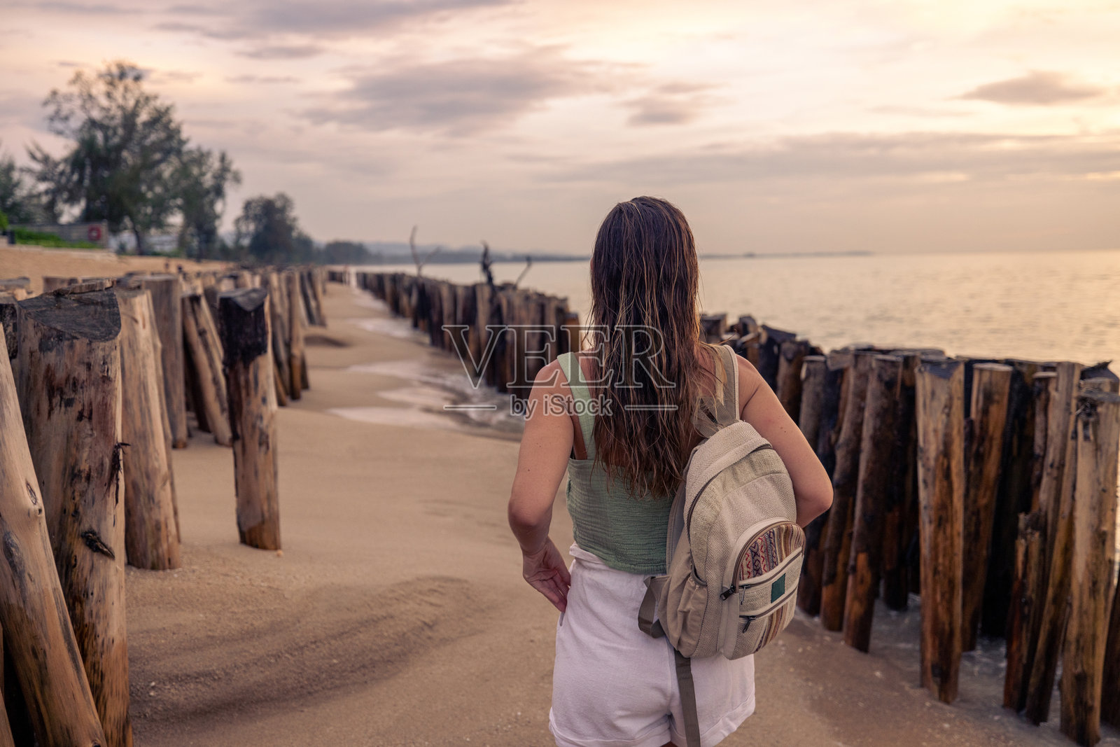 背着背包的女人在日落时分沿着海滩散步照片摄影图片