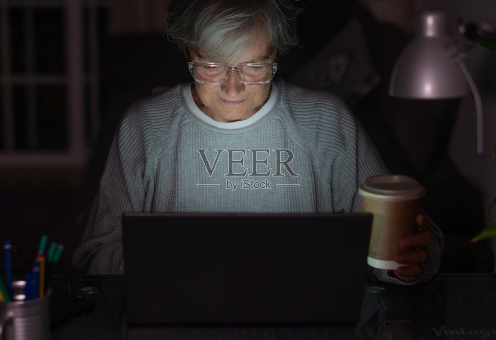 独自一人在家中的老年女性，夜晚使用笔记本电脑学习或工作，观看视频。照片摄影图片