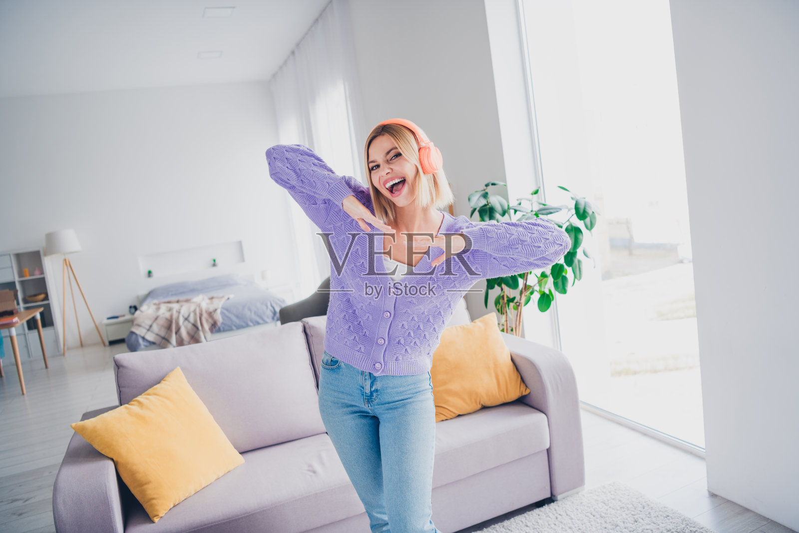 迷人的年轻女性在室内享受悠闲时光，戴着耳机，感受愉快的氛围和舒适的家居环境，坐在温馨的客厅里。照片摄影图片