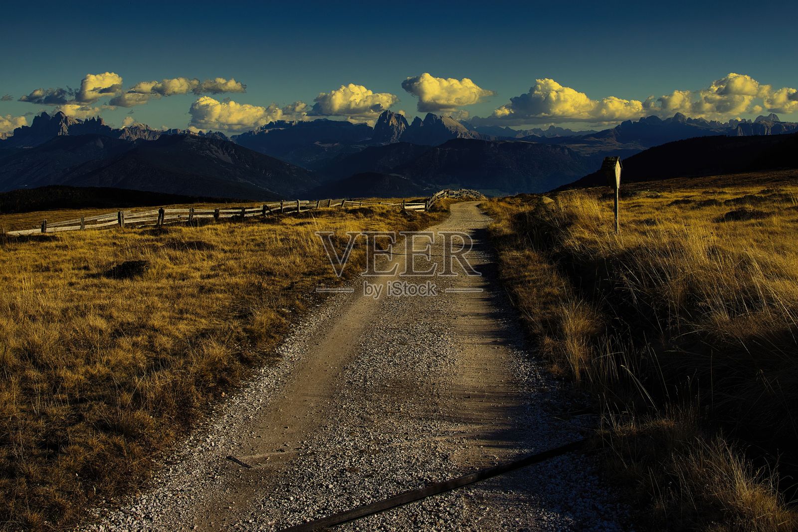 日落时分，穿过田野通往山脉的风景泥土小路。照片摄影图片