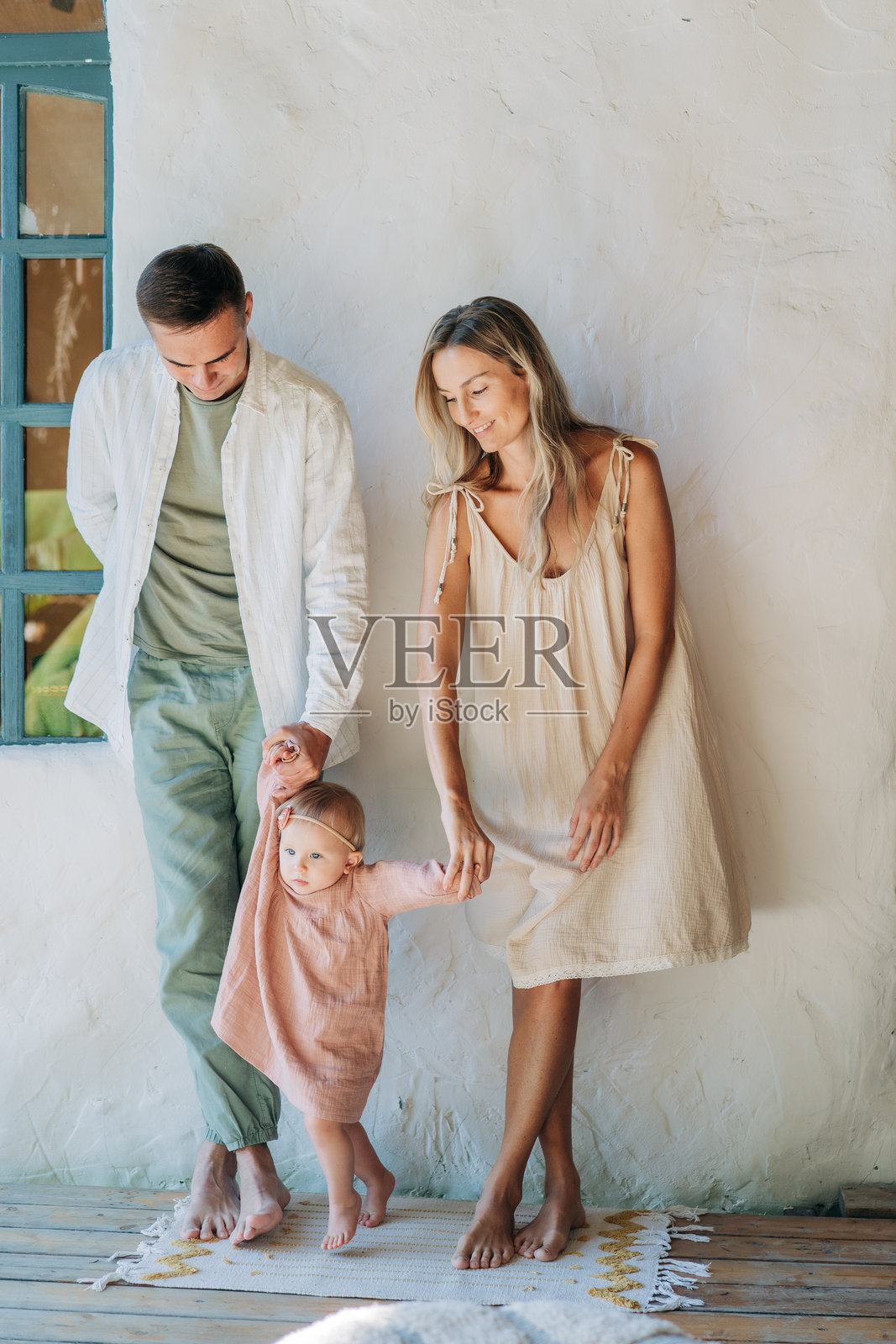 父母牵着小女儿的手，帮助她迈出第一步。照片摄影图片