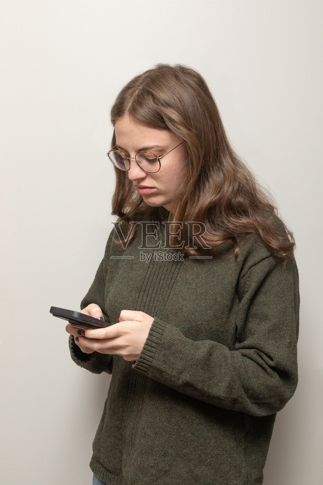 年轻女性在浅灰色背景下看着手机。照片摄影图片