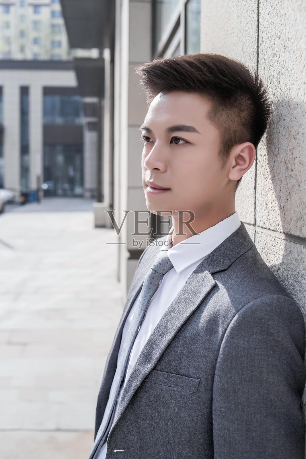 一位年轻的职业男性穿着西装站在外面，神情沉思。照片摄影图片