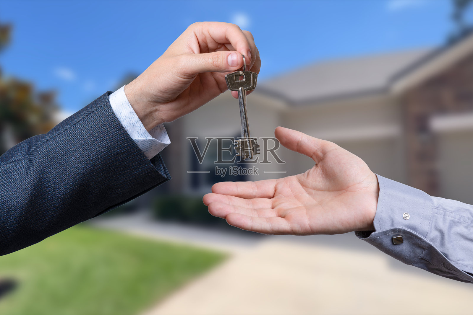 一只手将钥匙递给另一只手，背景是一栋房子。照片摄影图片