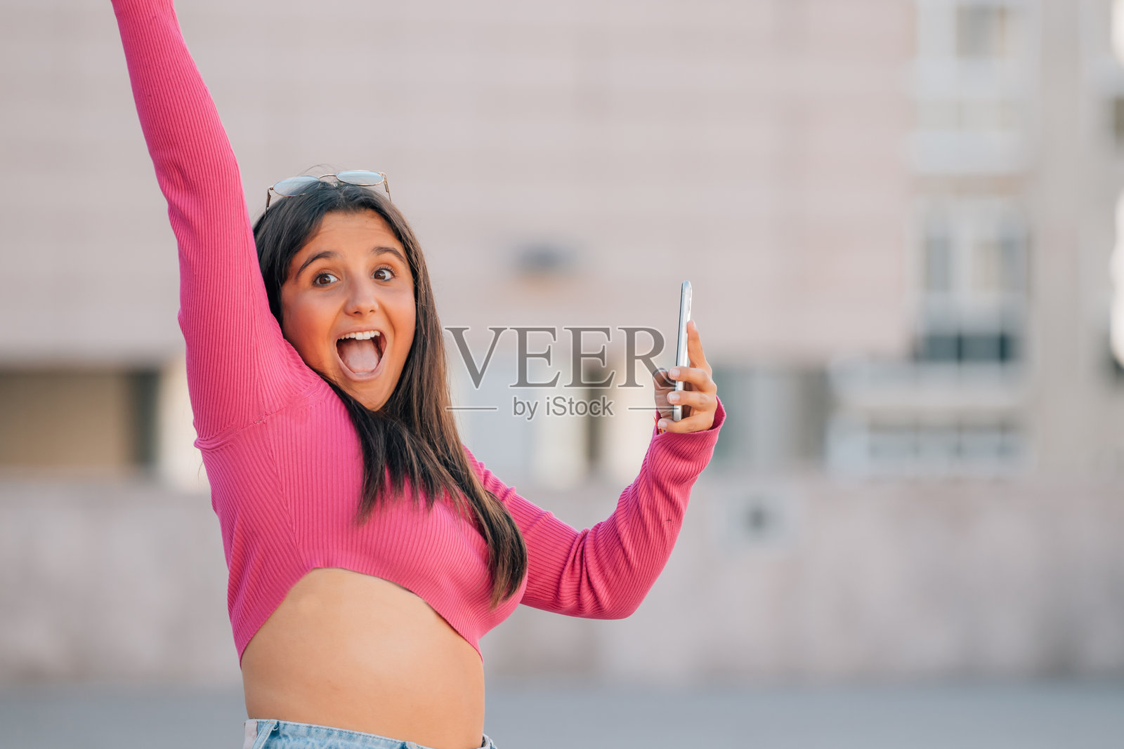 女孩在街上兴奋地尖叫，手里拿着手机。照片摄影图片