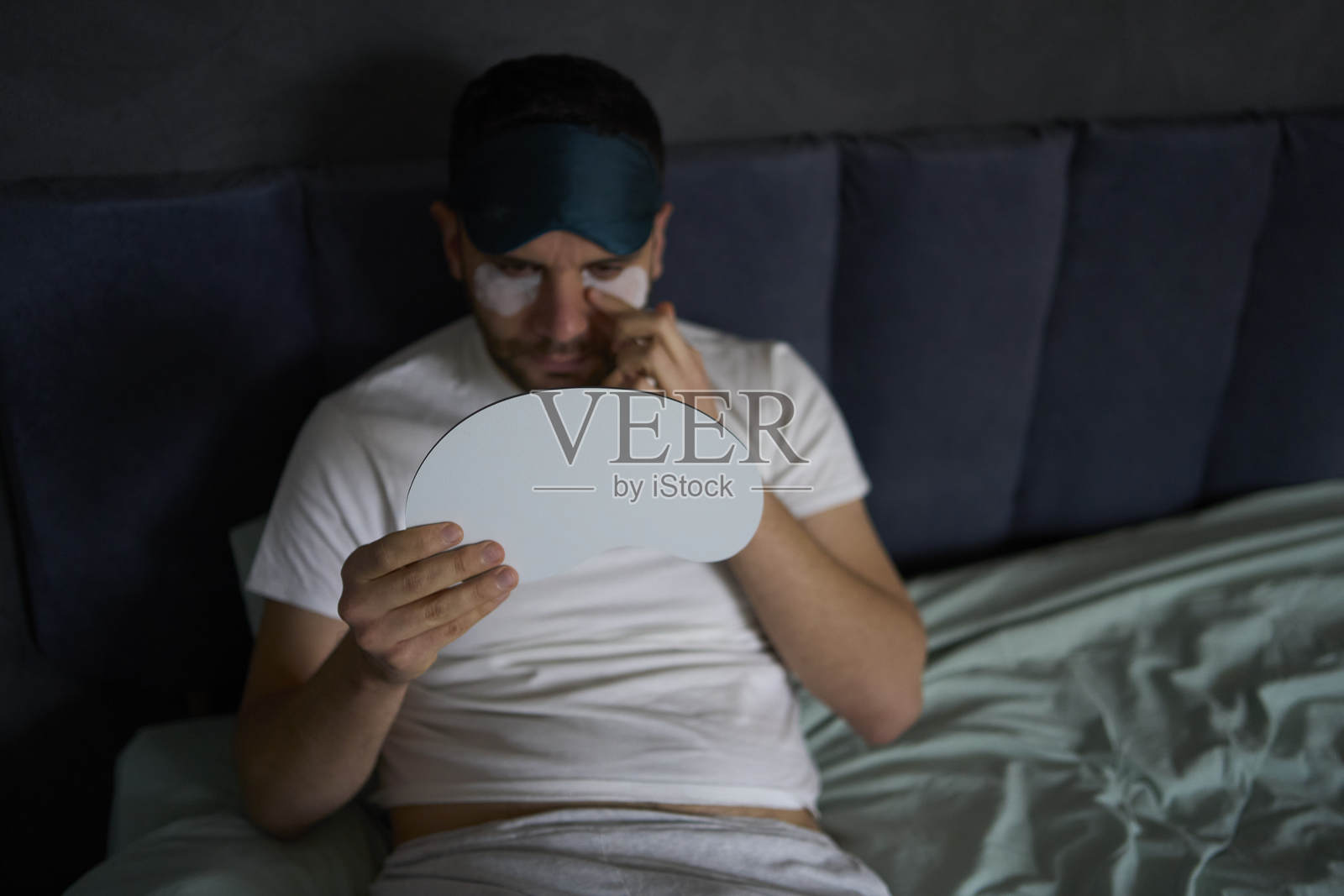 一名30岁的男子戴着丝绸睡眠面罩，在眼下贴上消肿和抗皱的贴片。照片摄影图片