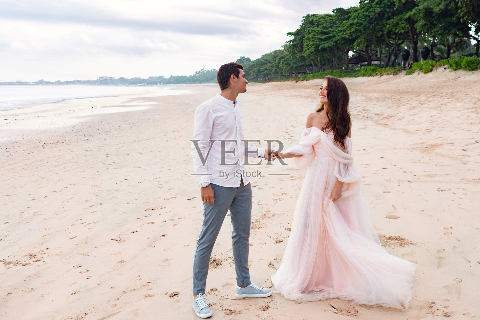 年轻的白人新婚夫妇在海滩上手牵手照片摄影图片