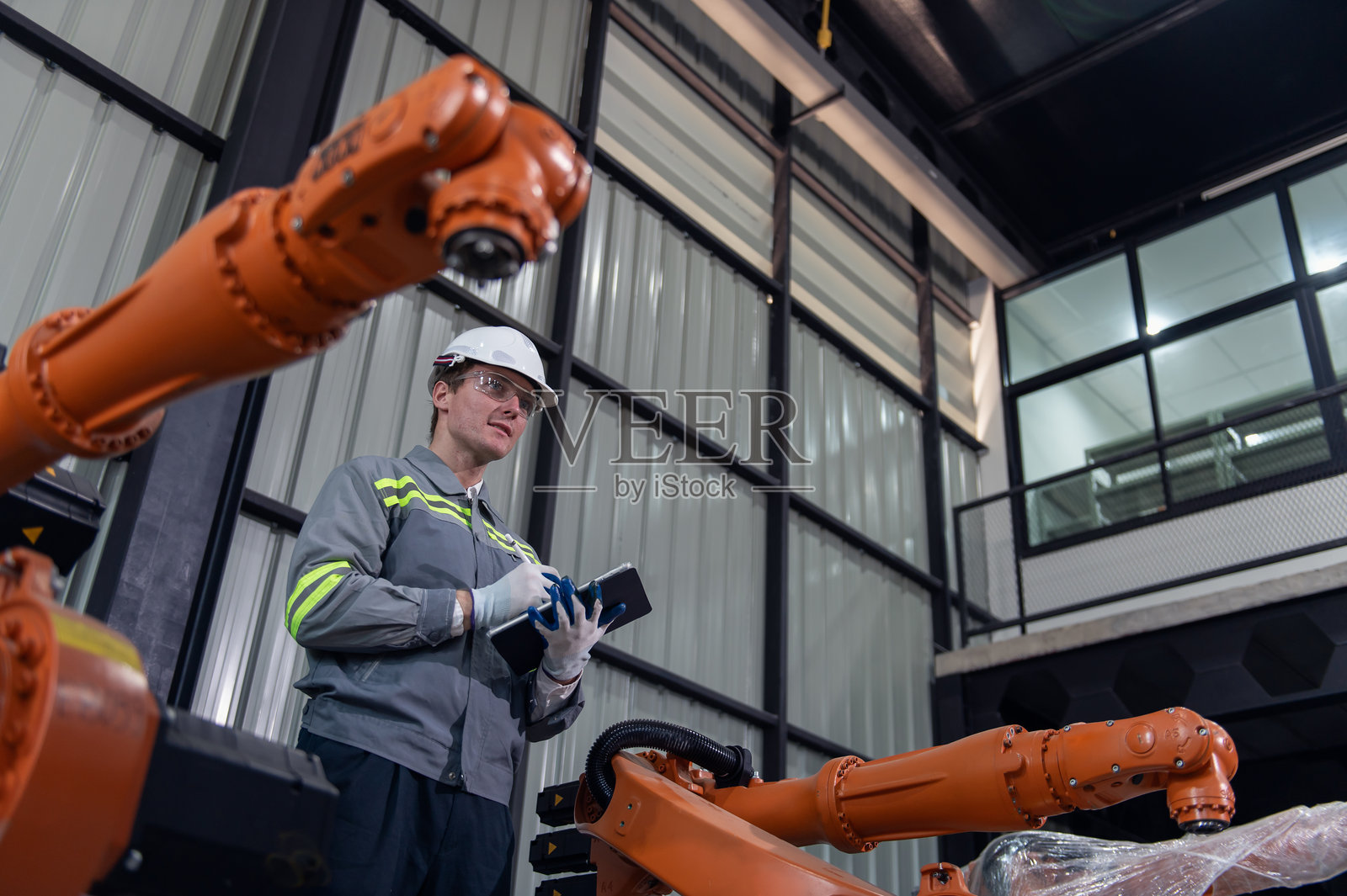 工程师站在工业工厂的机器人手臂旁，操作机器，技术工人检查电子设备的维修保养。照片摄影图片
