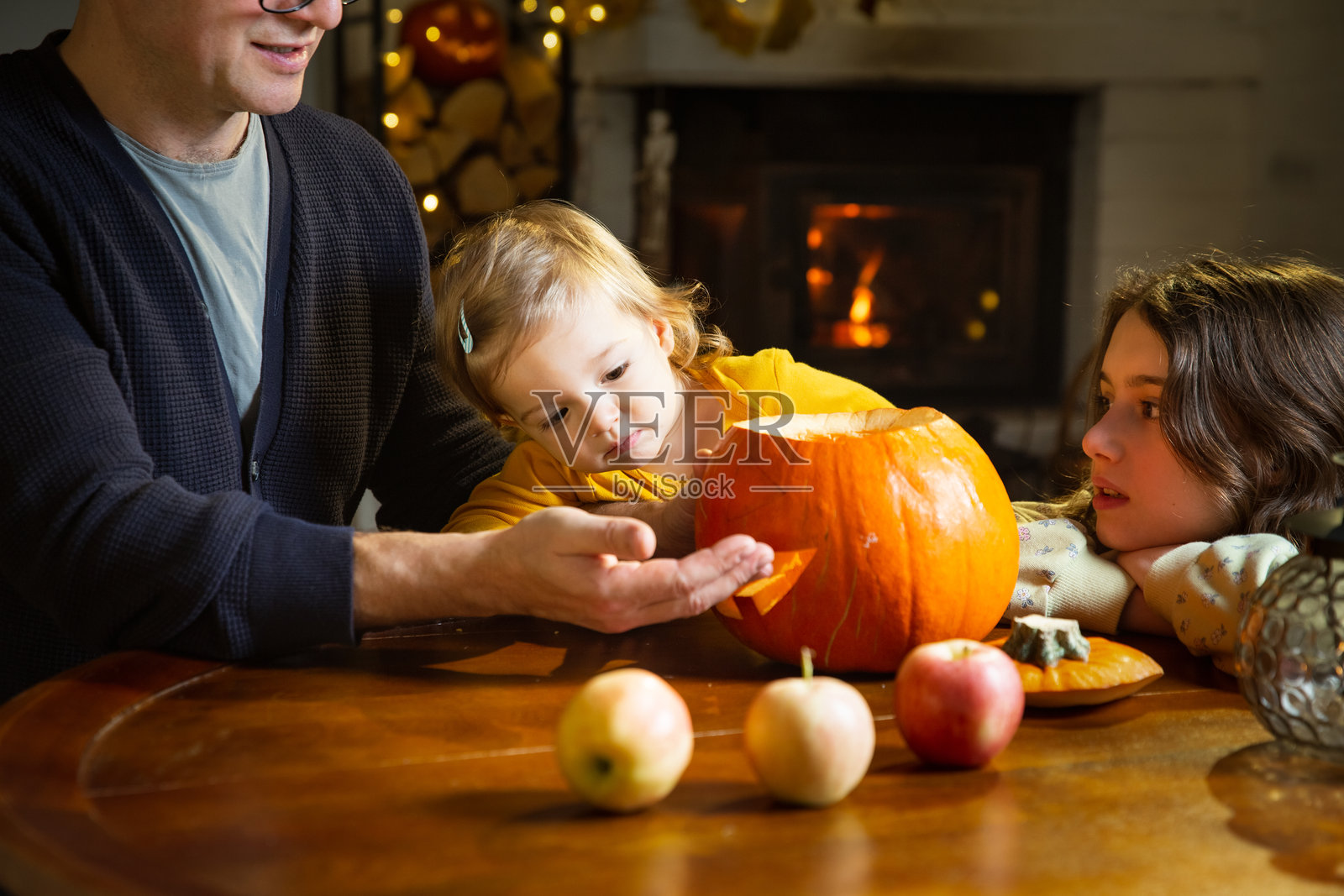 父亲和他的幼儿及女儿在家里雕刻南瓜灯，庆祝万圣节。在家进行有趣的手工艺和装饰。快乐的孩子们和他们的爸爸一起为节日做准备，装饰房子以迎接万圣节派对。照片摄影图片