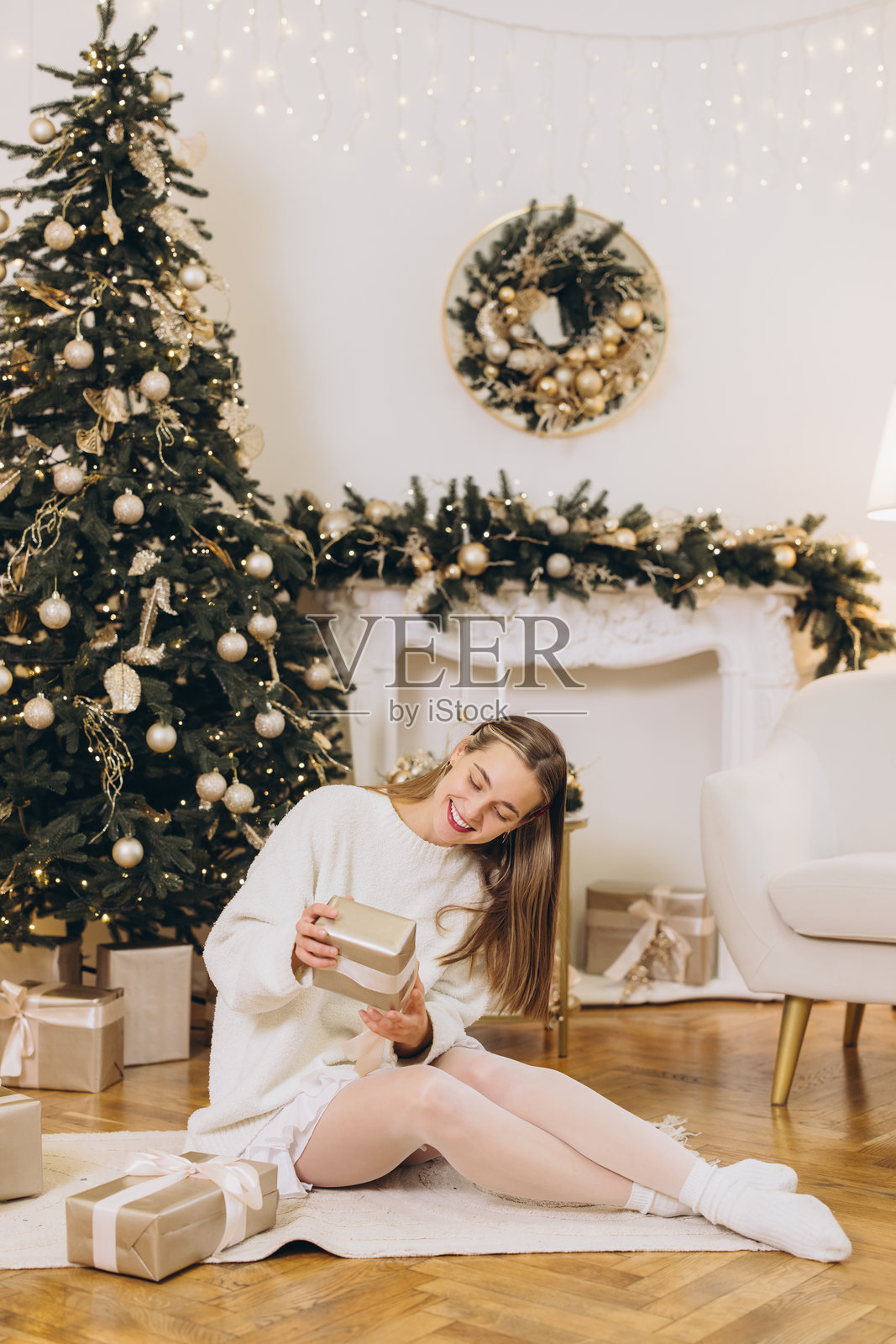 女人在装饰好的圣诞树和壁炉旁拿着圣诞礼物照片摄影图片