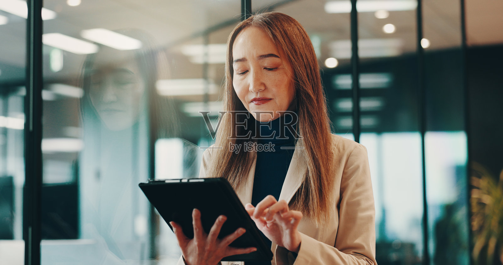 成熟的女性，在办公室夜间使用平板电脑进行商业网络、沟通和研究。经理，技术和报告获取，绩效评估和提案，使用KPI工具。照片摄影图片