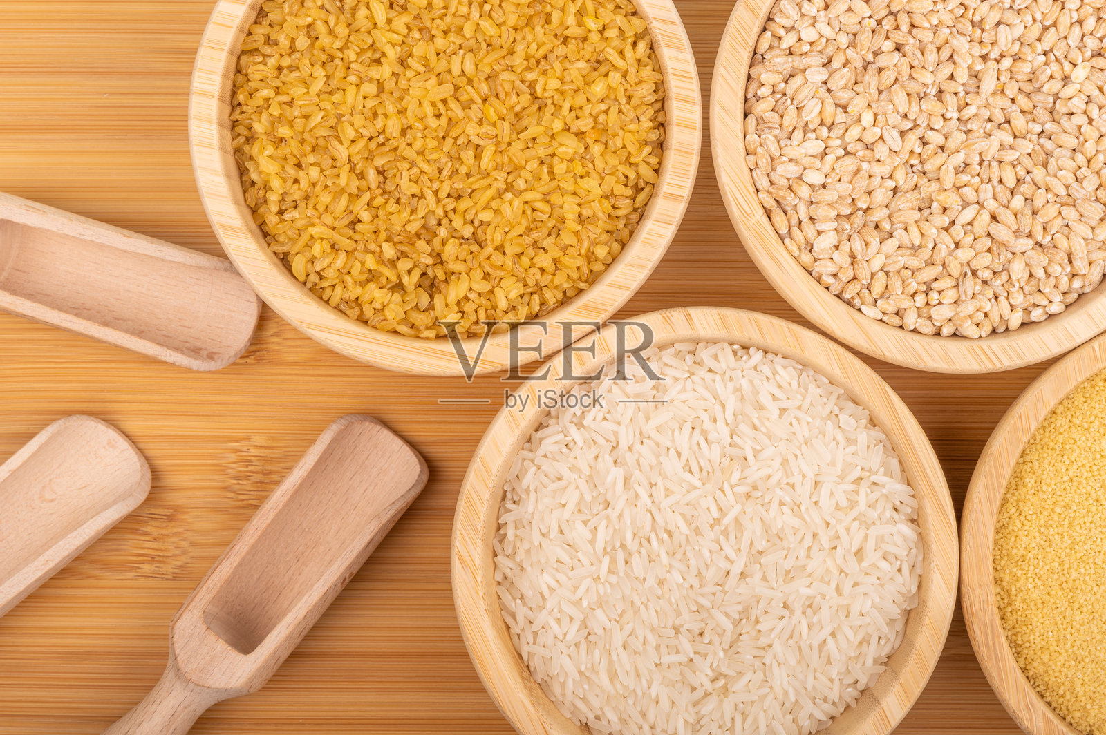 各种谷物放在木碗中，旁边有勺子，摆放在竹子表面上照片摄影图片