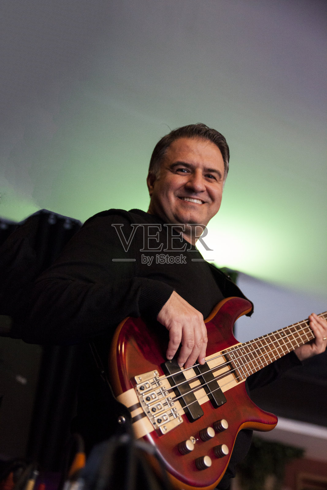 年轻男吉他手微笑着为现场表演排练，手中拿着贝斯吉他照片摄影图片